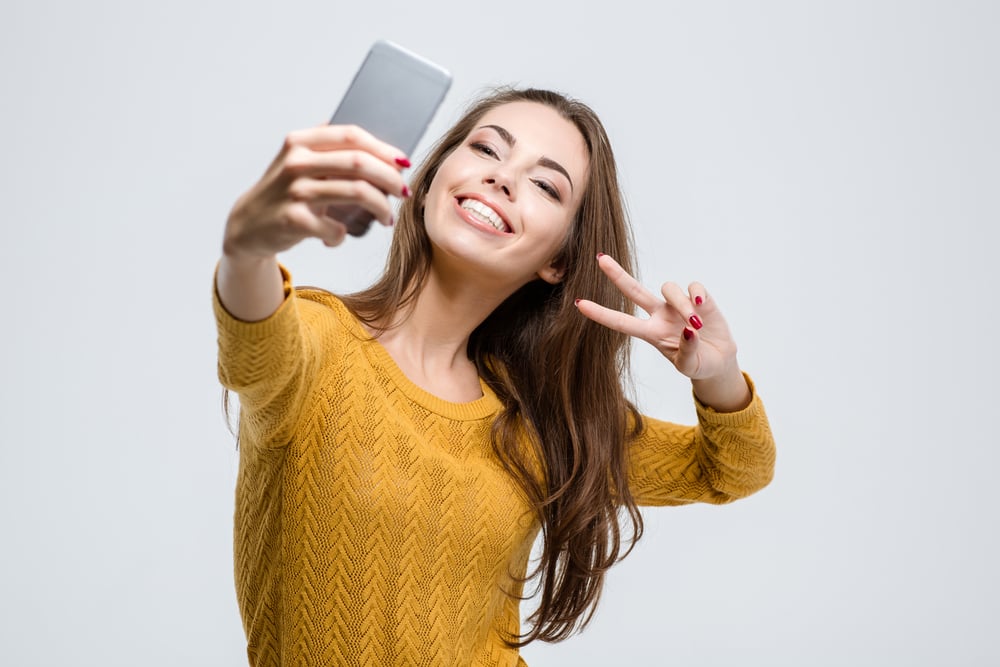 Portrait of a smiling cute woman making selfie photo on smartphone isolated on a white background